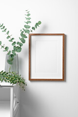 Blank poster frame mockup on white wall with natural eucalyptus decor