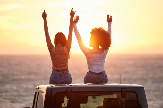 Sunset, women sitting on a car and at the beach with back view for carefree or peace. Freedom or adventure, summer vacation or holiday break and travel with female people at sea happy together