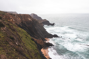 Fototapeta premium High limestone cliffs sinking into the Atlantic Ocean in the Algarve region, southwestern Portugal. Rainy weather. Wandering along the Fisherman Trail
