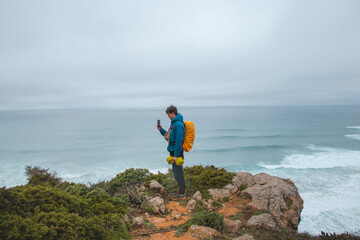 Obraz premium Adventurer wandering the Fisherman Trail in the Algarve region of Portugal takes pictures of the ocean, which has come to life during the rainy weather. The power of water