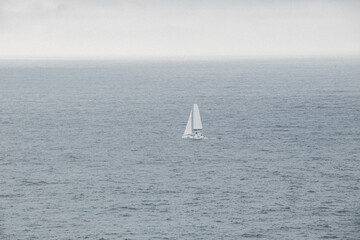 Obraz premium White sailfish sails through the stormy Atlantic Ocean in rainy weather in southern Portugal