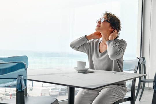 Brunette woman enjoying morning alone with fragrant coffee in cafe near panoramic seaside window.