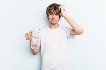 Young caucasian man holding a jar of water isolated on blue background being shocked, she has...