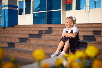 Little girl of elementary school student in modern school uniform outdoors with a bouquet of...