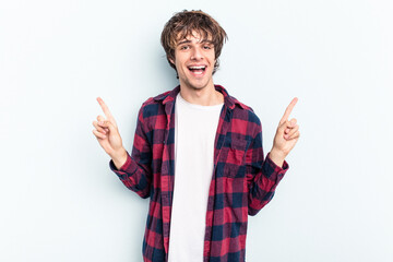 Young caucasian man isolated on blue background indicates with both fore fingers up showing a blank...