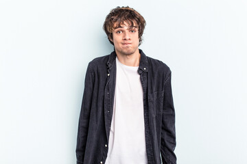Young caucasian man isolated on blue background shrugs shoulders and open eyes confused.