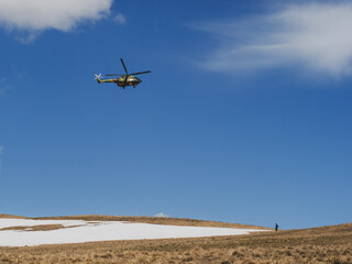 Fototapeta na wymiar Hélicoptère militaire en plein vol qui survole un randonneur au dessus d'un col enneigé 