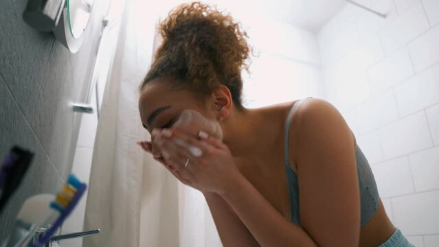 young woman in blue top and shorts washing face in bathroom sink in the morning side view slow motion health care, wellness treatment medicine daily routine free time