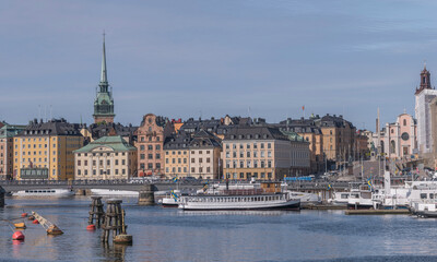 Fototapeta premium Boats moored at the jetties at the bridge Skeppsholmsbron, the old town Gamla Stan in the background, a sunny summer day in Stockholm