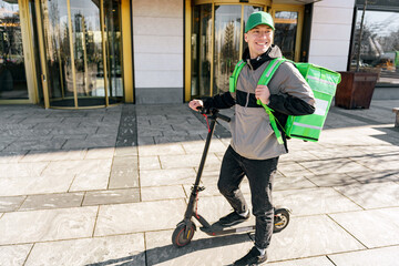 Uses an electric scooter to deliver the order, a satisfied male courier in a cap and with a thermo bag.