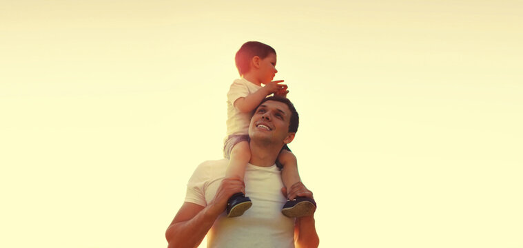 Happy smiling young father and little child son walking together outdoors on evening sunset sky on sunny day, family photo