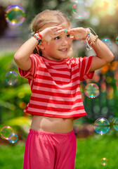 Portrait of а little toddler hippie  laughing girl covering her face with palms from the sun  in the garden summer time, freedom