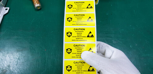 Hand holding ESD symbol label with antistatic gloves on static free workstation.