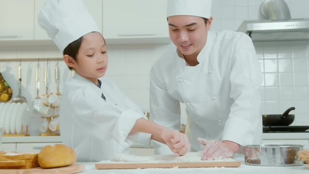 Young Asian father and his son wearing chef uniform baking together in kitchen at home