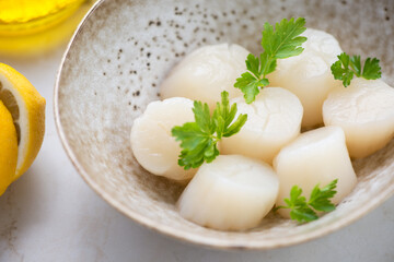 Closeup of raw fresh sea scallops with parsley in a beige bowl, selective focus, horizontal shot