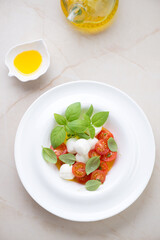 White plate with italian caprese salad on a beige marble background, vertical shot, high angle view