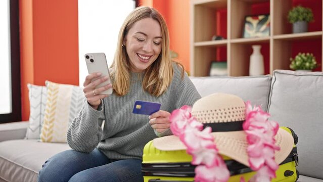 Young blonde woman shopping flight with smartphone and credit card sitting on sofa at home