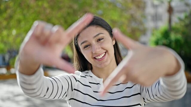 Young beautiful hispanic woman smiling confident doing frame gesture with hands at park