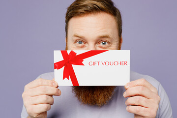 Close up young redhead bearded man he wear violet t-shirt casual clothes hold gift certificate coupon voucher card for store isolated on plain pastel light purple background studio. Lifestyle concept.