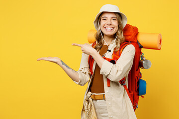 Young fun woman carry backpack with stuff mat point finger on empty palm isolated on plain yellow...
