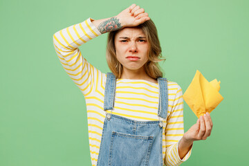 Sick unhealthy ill allergic sad woman has red watery eyes runny stuffy sore nose suffer from allergy trigger symptoms hay fever hold napkin isolated on plain pastel green background studio portrait.