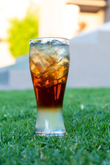 Long Island cocktail with a straw on green grass. Mixed alcoholic cocktail