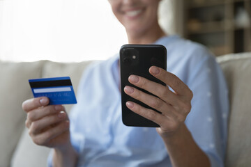 Happy bank client woman holding credit card and mobile phone, using financial commerce application, making online payment, money transaction, shopping on Internet. Cropped shot, hands close up