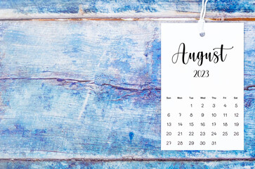 The August 2023 calendar page hanged with white rope on old blue wooden background.
