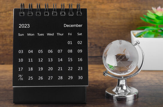 The December 2023 desk calendar for 2023 year Black color with a crystal globe against a wooden table background.