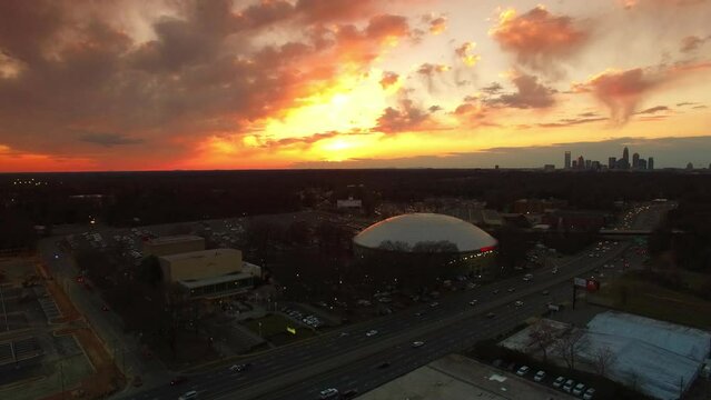 Aerial Shot Of Bojangles Coliseum By Freeway At Sunset, Drone Descending Forward Over City Against Cloudy Orange Sky - Charlotte, North Carolina