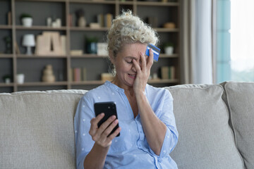 Worried senior mature woman holding smartphone and credit card, getting frustrated, stressed,...