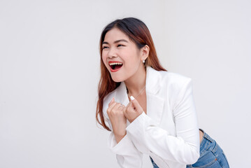 An eager young woman with fist raised to chest in excitement and mouth open wide. Isolated on a white background.