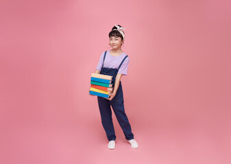 Back to school. Schoolgirl asian student holding book isolated on pink studio background. School...