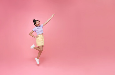 Fototapeta na wymiar Happy Asian woman smiling jumping and pointing finger presenting to copy space isolated over pink studio background.