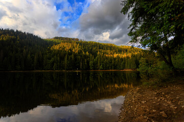 Obraz premium Majestic mountain lake surrounded by verdant woods and towering peaks, tranquil twilight