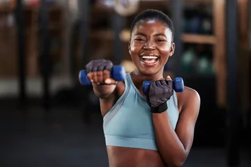 Fotobehang Sportschool Portrait of boxer, dumbbell or happy black woman training, exercise or workout for a strong punch or power. Smile, face or African girl boxing with dumbbells, weights or exercising in fitness gym  © Michael Cunningham/peopleimages.com