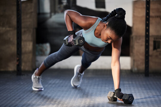 Gym workout, dumbbells and a black woman on the floor for fitness, exercise and training for sports. Strong, healthy and an African athlete with weights for strength, muscle and health at a club