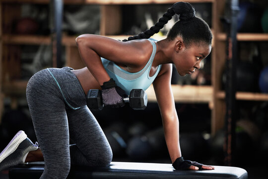 Gym, dumbbell or strong black woman on bench training, exercise or workout for powerful arms or muscles. Wellness, health club or African girl lifting weights or exercising shoulders with fitness