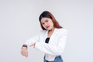 An angry young woman pointing at her watch while looking at the camera. Isolated on a white background. - obrazy, fototapety, plakaty