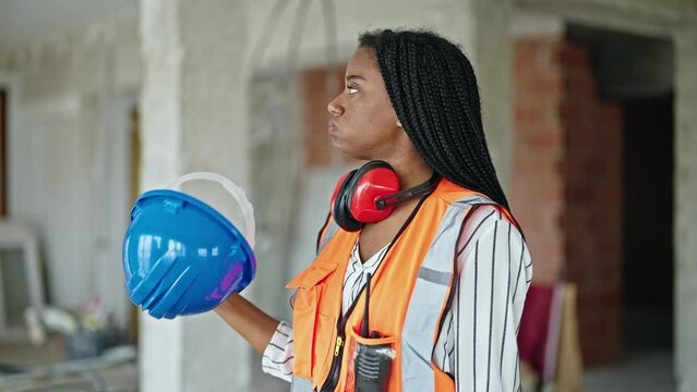 African american woman builder sweating using hardhat as a handfan at construction site
