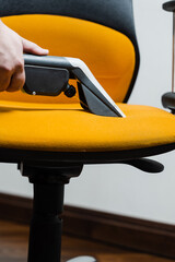 Housekeeper is extracting dirt from armchair using dry cleaning extractor machine. Cleaning yellow...