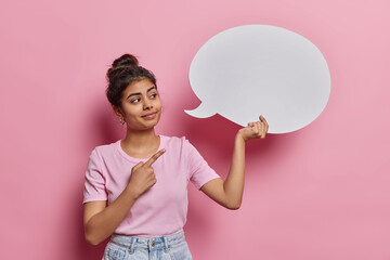 Horizontal shot of pretty young Indian woman points at blank speech bubble for writing your...