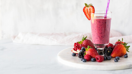 A mixed berry smoothie surrounded by berries, ready for drinking.