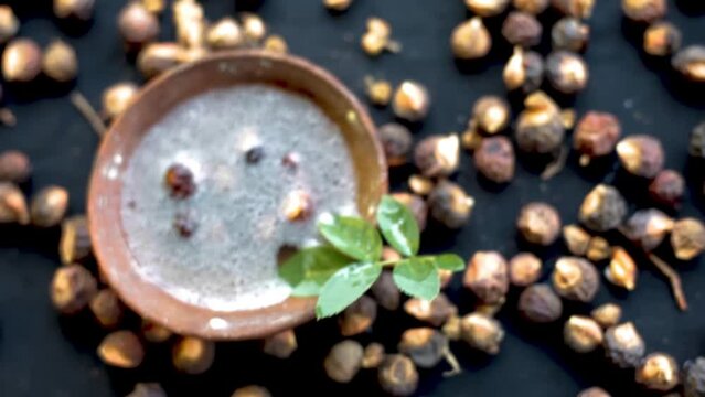 Sapindus mukorossi or soapnuts or areetha on a black-colored surface along with its fermented water used for hair care and cosmetics.

