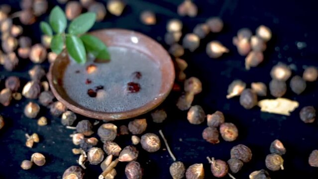 Sapindus mukorossi or soapnuts or areetha on a black-colored surface along with its fermented water used for hair care and cosmetics.
