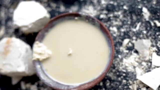 Multani mitti or Fuller's earth on a black surface and its paste in a clay bowl used for face masks and face packs for naturally glowing skin. HD footage in 24FPS.