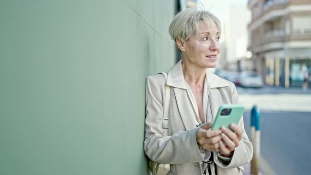 Middle age blonde woman smiling confident using smartphone at street