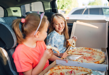 Portrait of two positive smiling sisters eating just cooked italian pizza sitting in child car...