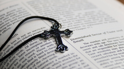 Shiny metal cross with black sling on old book to  recall the kindness of Jesus Christ for all of...