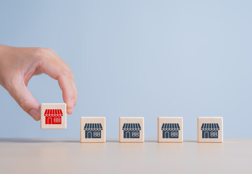 Franchise Business marketing concept. Hand holding a wooden cube red store icon with other wood blocks. The idea for business sale growth and expansion shop concept. Development of retailing business.